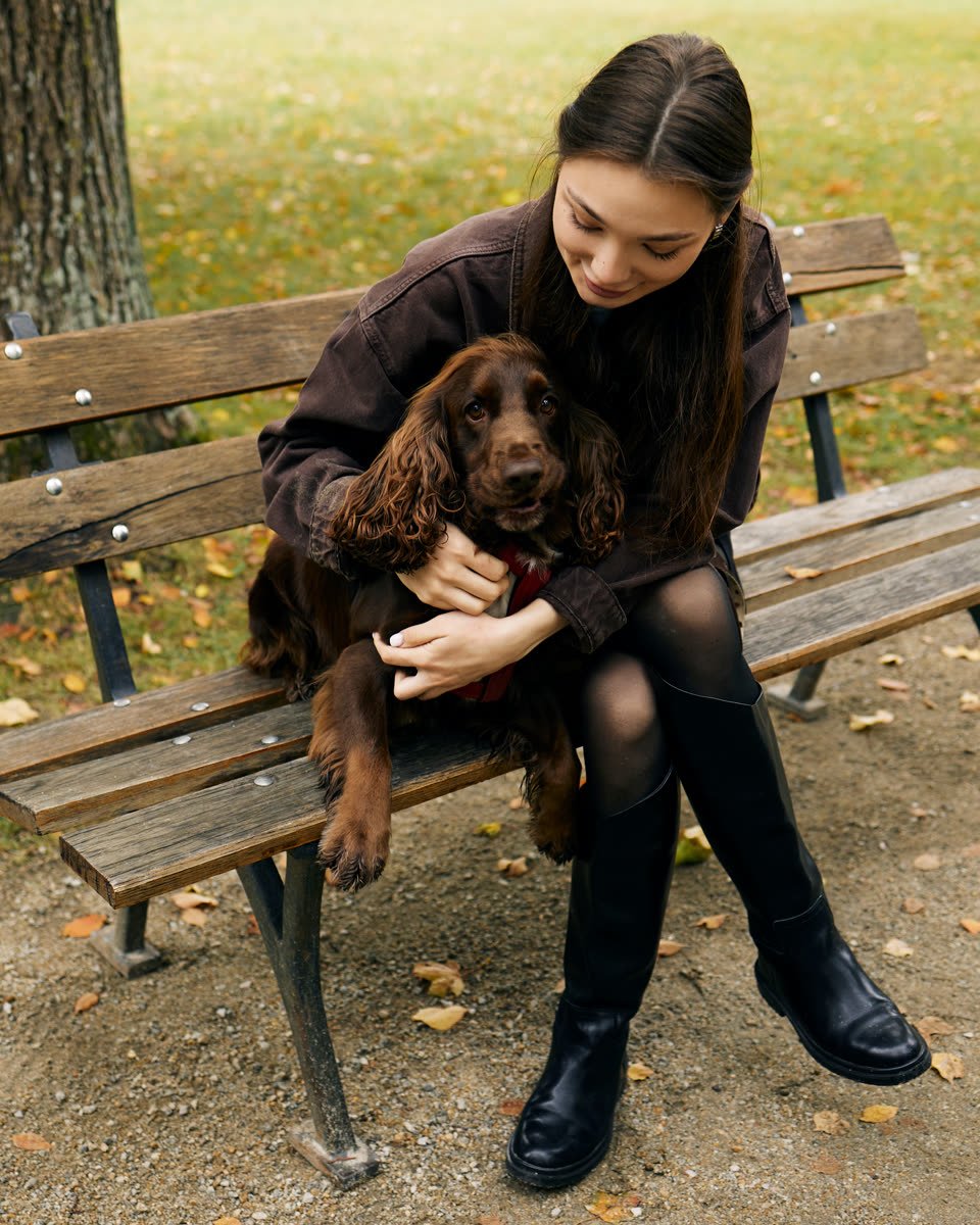 Šeimininkė glosto kokerspanielį ant parko suoliuko